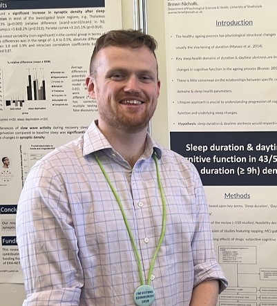 A smiling man, in a shirt, in front of an academic poster